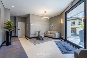 Un moderno vestíbulo de hotel con una recepción, un sofá, una planta en maceta y un amplio ventanal con vistas al exterior.