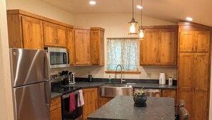Una cocina moderna con armarios de madera, electrodomésticos de acero inoxidable, una isla central con taburetes de bar e iluminación colgante.
