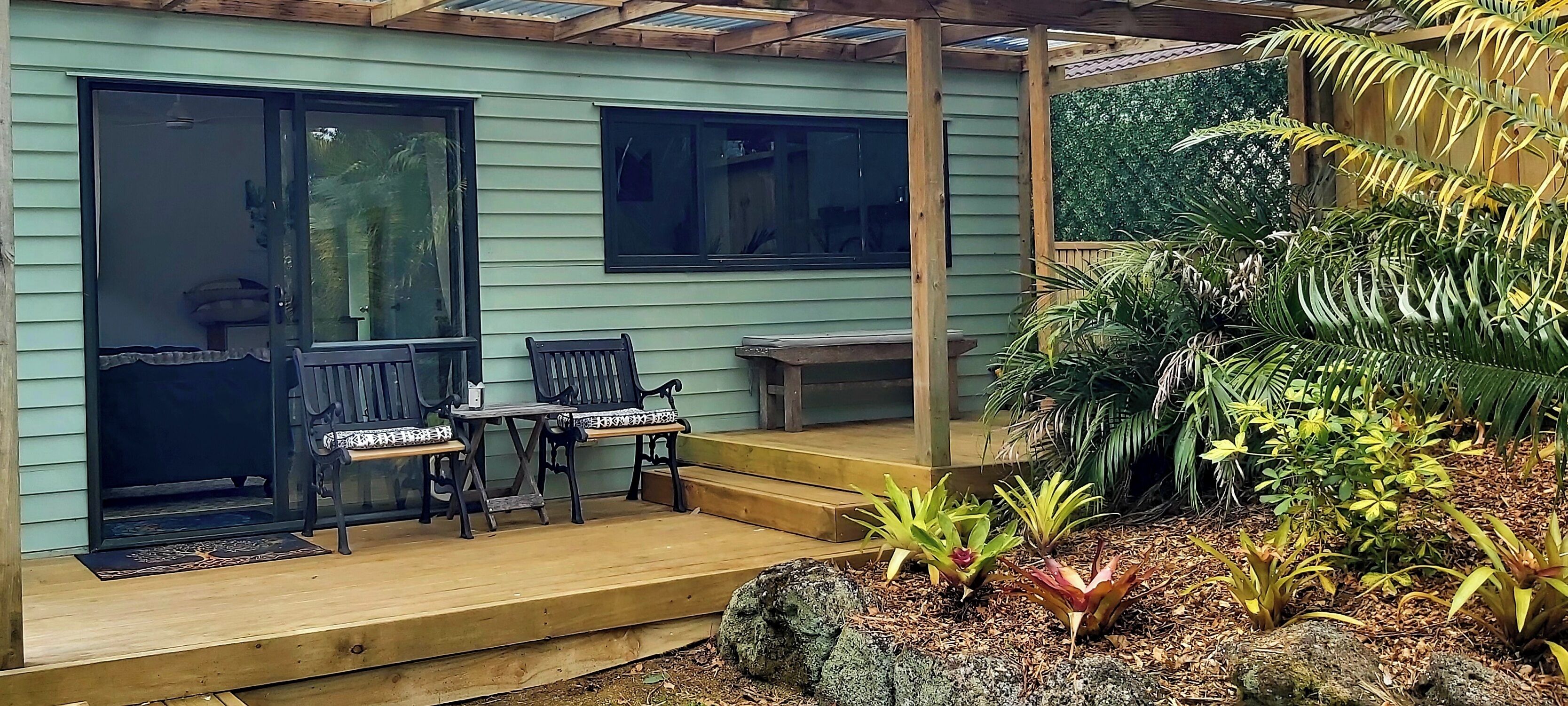A wooden deck with two benches and a small table, surrounded by lush greenery and plants.