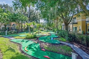 Ein Minigolfplatz mit mehreren grünen Putting-Bereichen, umgeben von Bäumen und einem Zaun.