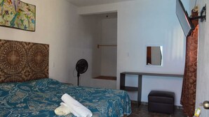 Une chambre d’hôtel avec un lit, un bureau, un ventilateur et un miroir.