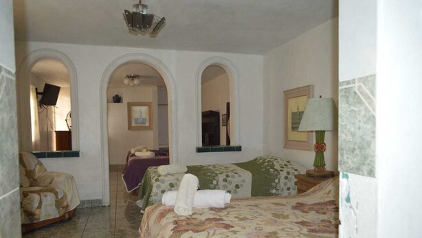 Une chambre d’hôtel avec deux lits, un coin salon et une salle de bain visible à travers une arche.