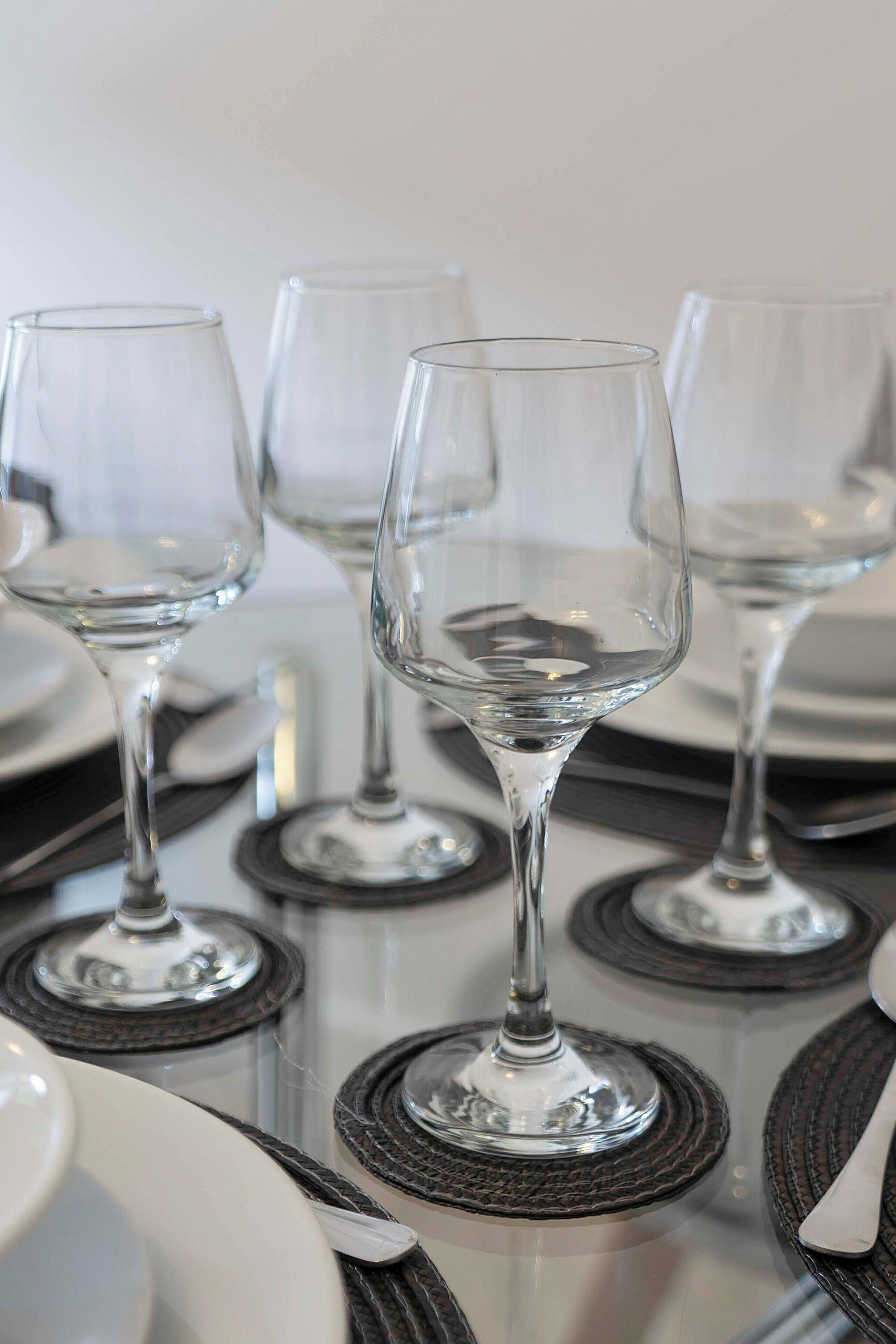 A table set with wine glasses and plates, with a clear glass centerpiece.