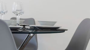 A modern dining area with a glass table, grey chairs, and a white wall in the background. - Stylish 4bed Home Free Parking 20 Min to Edinburgh (Livingston)