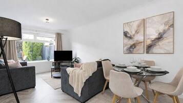 A modern living room with a grey sofa, a dining table set for four, and abstract art on the wall.