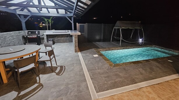 Een terras buiten met een zwembad, een barbecueplek en een hangstoel.
