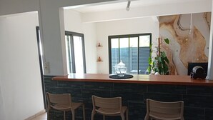 Een keuken met een bar, drie krukken, een groot raam en een decoratieve wand.