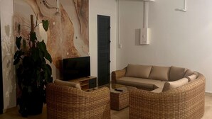Een woonkamer met een grote televisie, een bank en een salontafel. Er staat een plant en een muur met een marmer dessin.