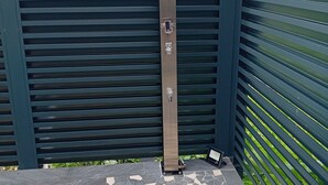 Een metalen constructie met een bedieningspaneel, voor een groene hekken en een betegelde vloer met een geometrisch patroon.