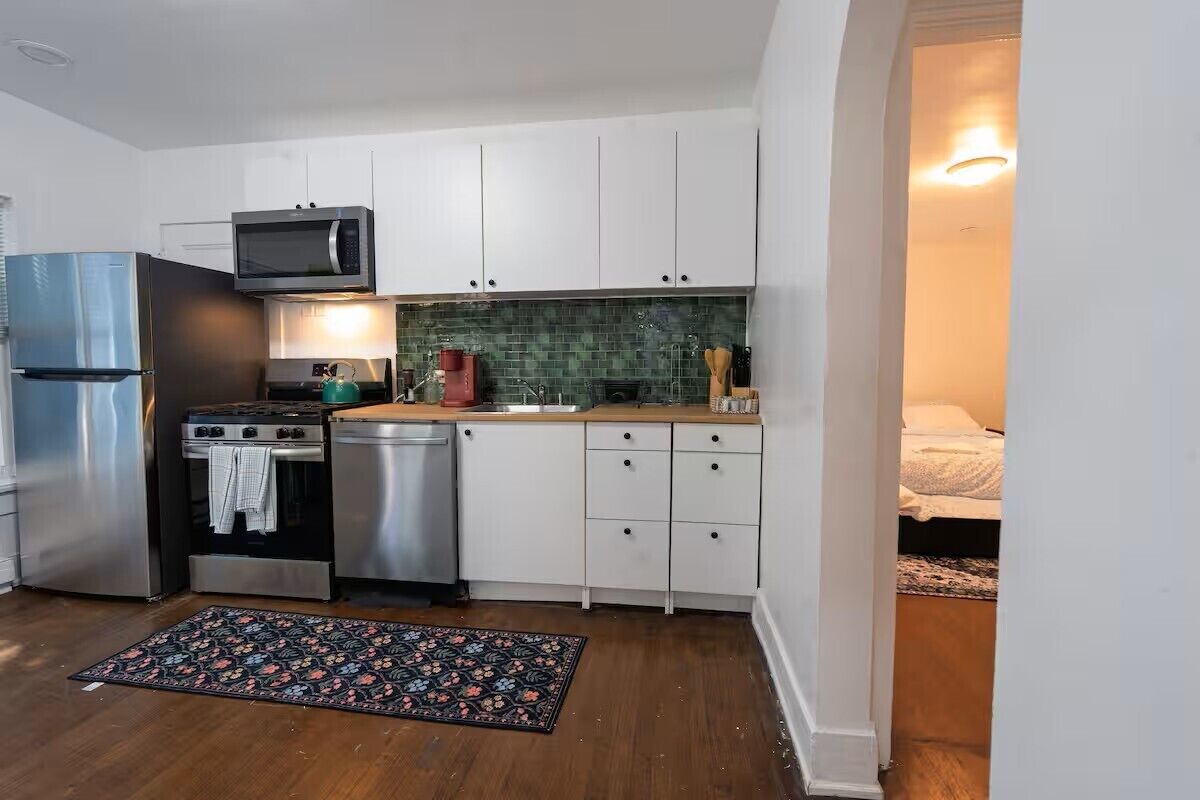 A compact kitchen with white cabinets, a stainless steel refrigerator, a microwave, a stove, and a dishwasher.