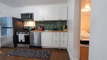 A compact kitchen with white cabinets, a stainless steel refrigerator, a microwave, a stove, and a dishwasher.