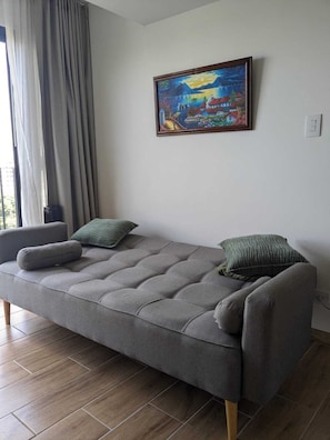 Ein modernes Wohnzimmer mit einem grauen Sofa, zwei grünen Kissen und einem Landschaftsbild an der Wand.