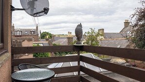 Een houten terras met een tafel, stoelen, een schotelantenne en een decoratief vogelbeeldje.