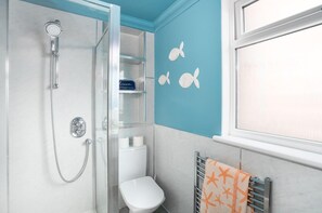 Casa de banho com chuveiro, sanita e porta-toalhas com toalha estampada com estrelas-do-mar.