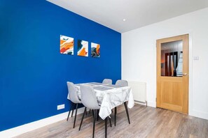 A dining area with a blue accent wall, a wooden door, and a white radiator. - Airport Apartment - Aberdeen - Free Parking (Aberdeen)