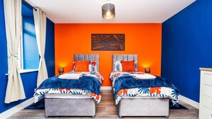 A bedroom with two beds, a large window with curtains, a wall-mounted light fixture, and a decorative wall piece. - Airport Apartment - Aberdeen - Free Parking (Aberdeen)