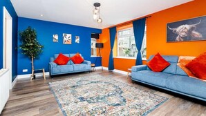 A modern living room with blue sofas, a patterned rug, and a large window with curtains. - Airport Apartment - Aberdeen - Free Parking (Aberdeen)