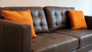 Ein dunkelbraunes Ledersofa mit zwei orangenen Kissen.