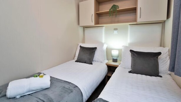 Una habitación de hotel con dos camas, una mesita de noche con lámpara y un estante de madera sobre las camas.