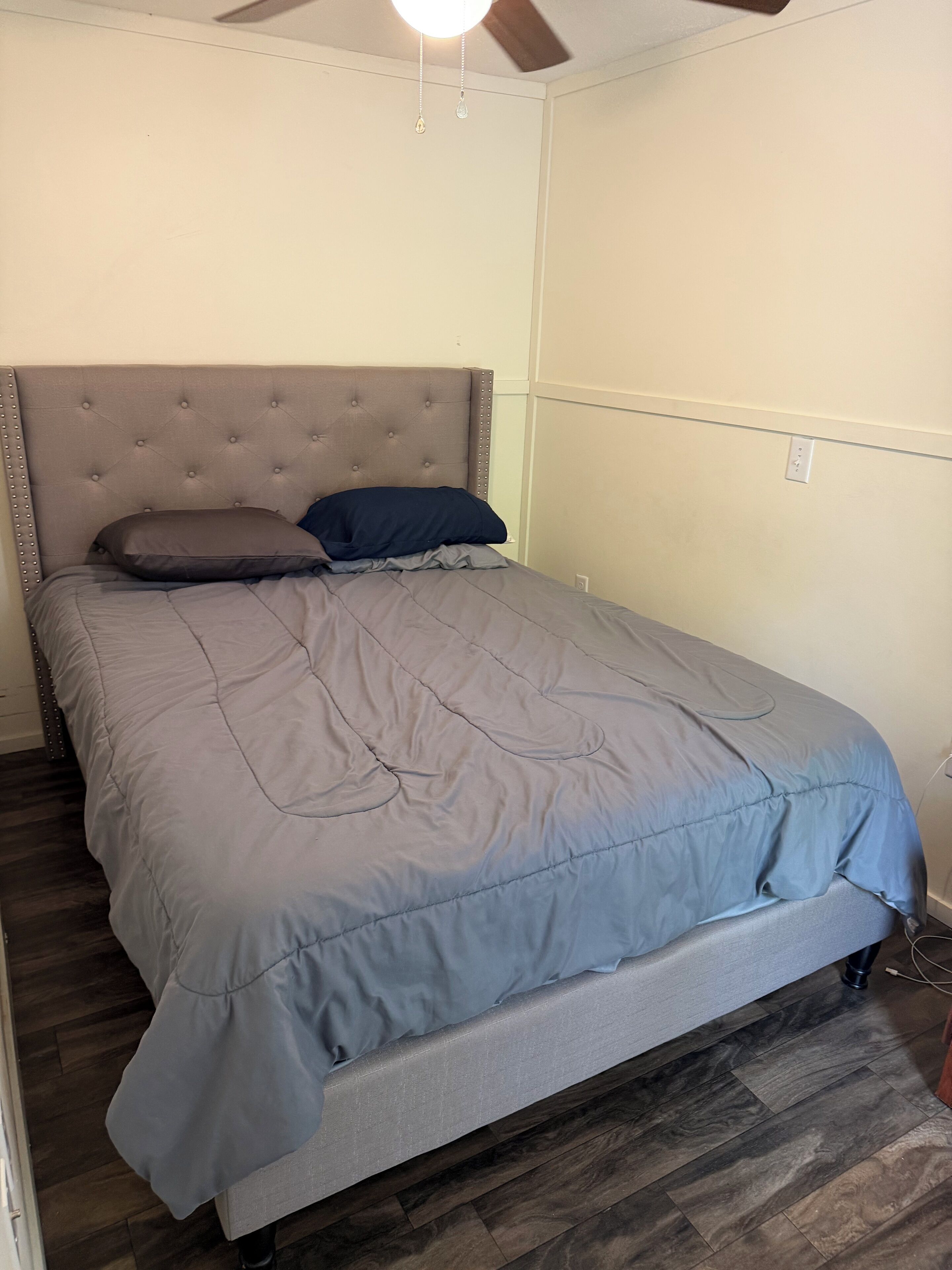 A bedroom with a bed, a ceiling fan, and a wooden floor.