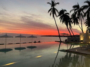 A poolside area with lounge chairs and umbrellas, overlooking a body of water during sunset. - Oceanfront apartment, an oasis with spectacular views. (Bucerías)