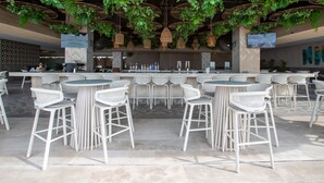 Un área de bar al aire libre con varios arreglos de asientos, una barra y plantas colgantes.