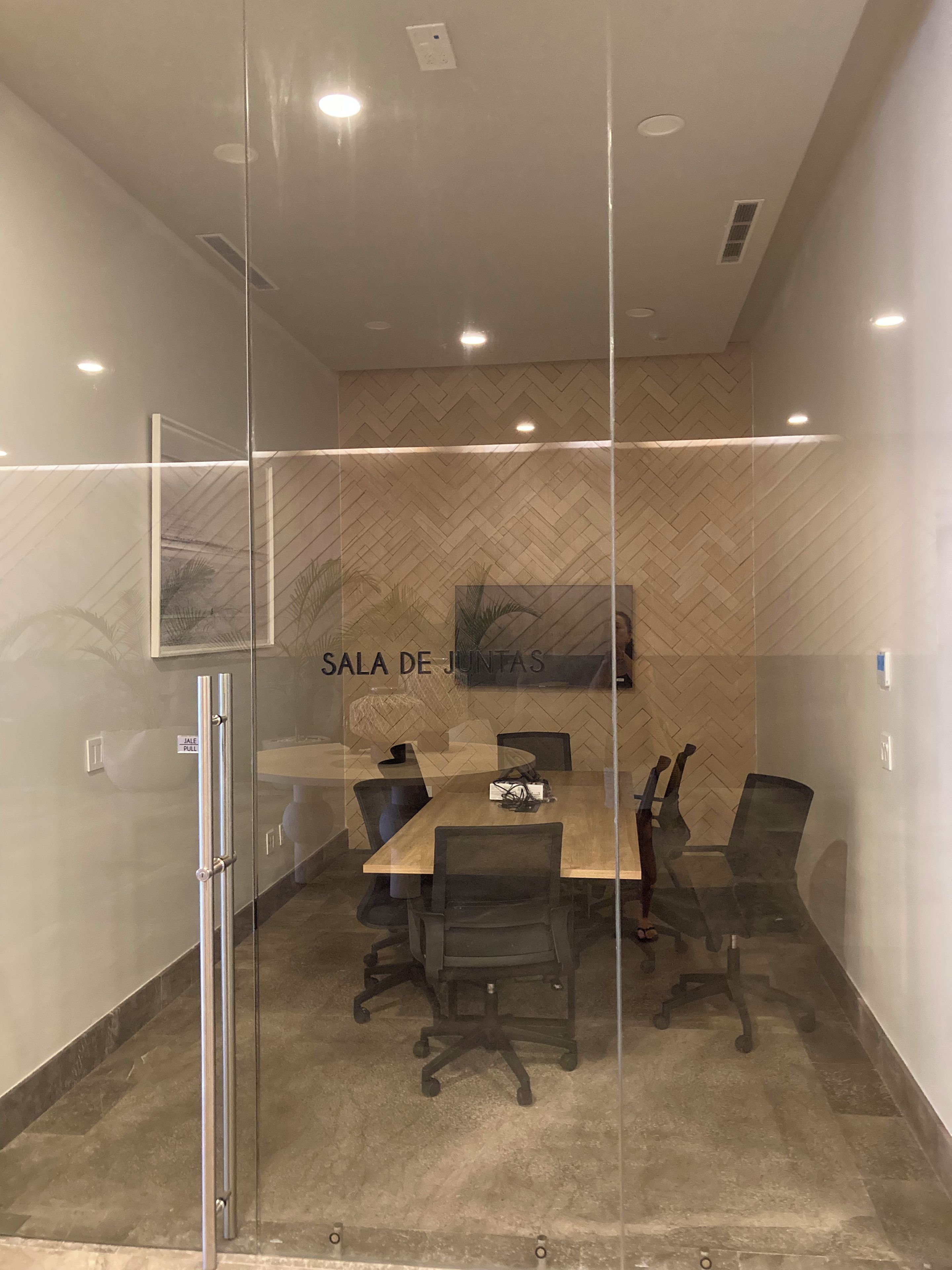 A conference room with a glass partition, a wooden table, and office chairs.