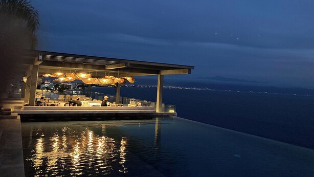 Una piscina infinita con vistas al mar y un área exterior cubierta con asientos e iluminación.