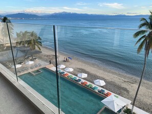 A pool with lounge chairs and umbrellas, overlooking a beach and a mountainous landscape. - Oceanfront apartment, an oasis with spectacular views. (Bucerías)