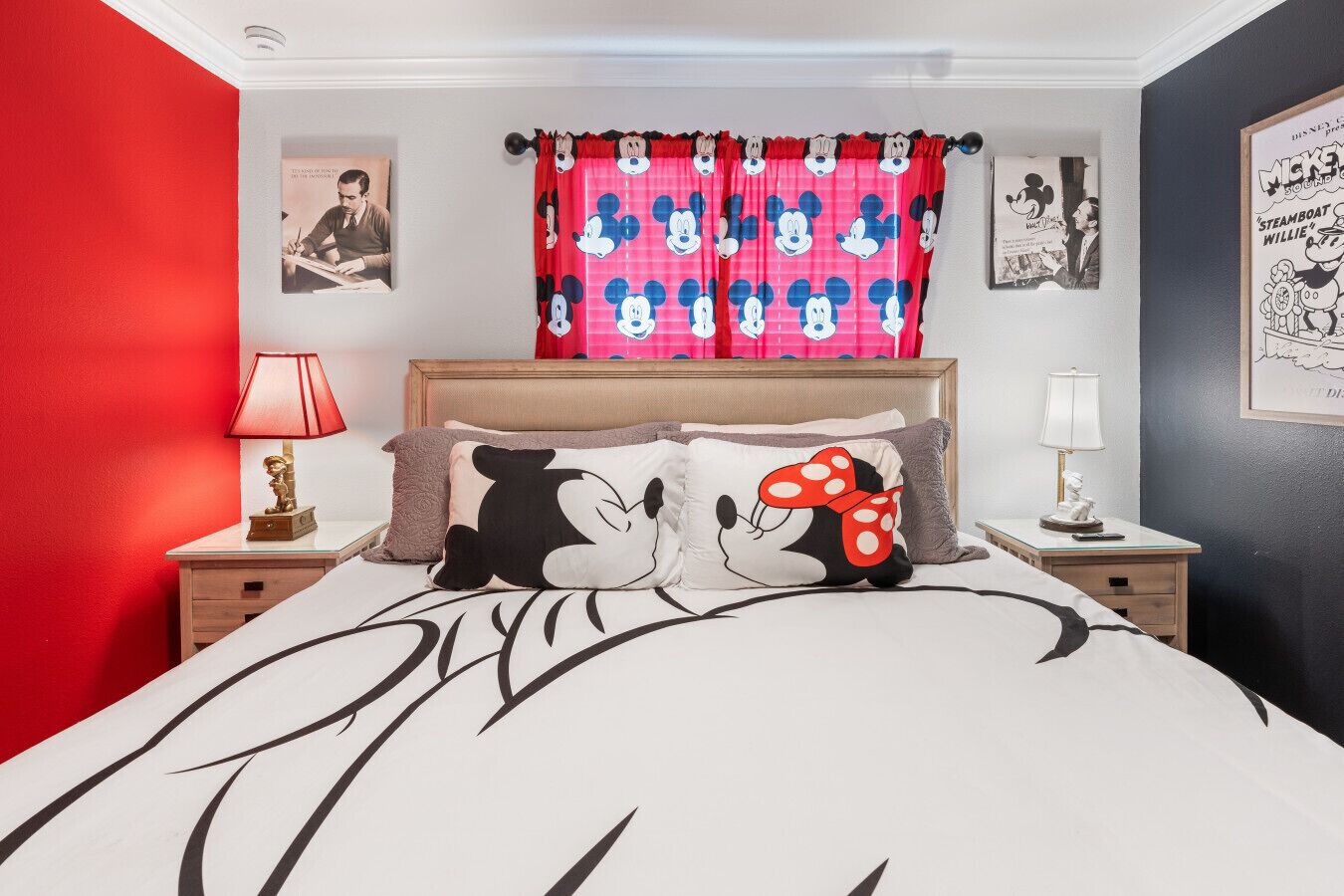 Et soveværelse med en seng, hovedpuder med Mickey Mouse og Minnie Mouse, en rød væg og et Mickey Mouse plakat på væggen.