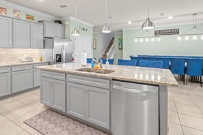 A modern kitchen with granite countertops, stainless steel appliances, and blue upholstered chairs at a dining table. - Luxury 10BR Windsor Island Home, Pool, Game Room (Davenport)
