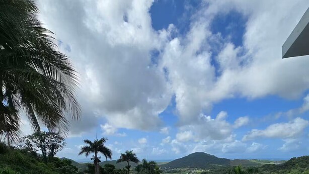 A terrace with two lounge chairs and a small stool, overlooking a lush landscape with hills and a clear sky. - Piscina Vista II Ocean & Mountain Views with Solar (Ceiba)