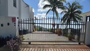 A gated entrance with a 'Reserved Parking' sign, palm trees, and a mountainous backdrop. - Piscina Vista II Ocean & Mountain Views with Solar (Ceiba)