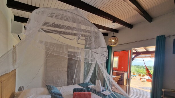 A bed with a canopy, a hanging light fixture, and a view of the outdoors. - LE MALIATA "Villa Vue Mer piscine Privée" (Sea View Private Pool) (Saint-François)