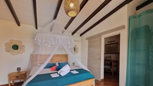 A neatly made bed with a canopy, a bedside table with a lamp, and a bathroom visible through an open door. - LE MALIATA "Villa Vue Mer piscine Privée" (Sea View Private Pool) (Saint-François)