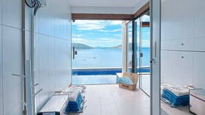 A corridor with a view of a large body of water, a pool, and a seating area with cushions. - Luxury Oceanfront Villa with Infinity Pool, Sauna & Total Privacy (Arraial do Cabo)
