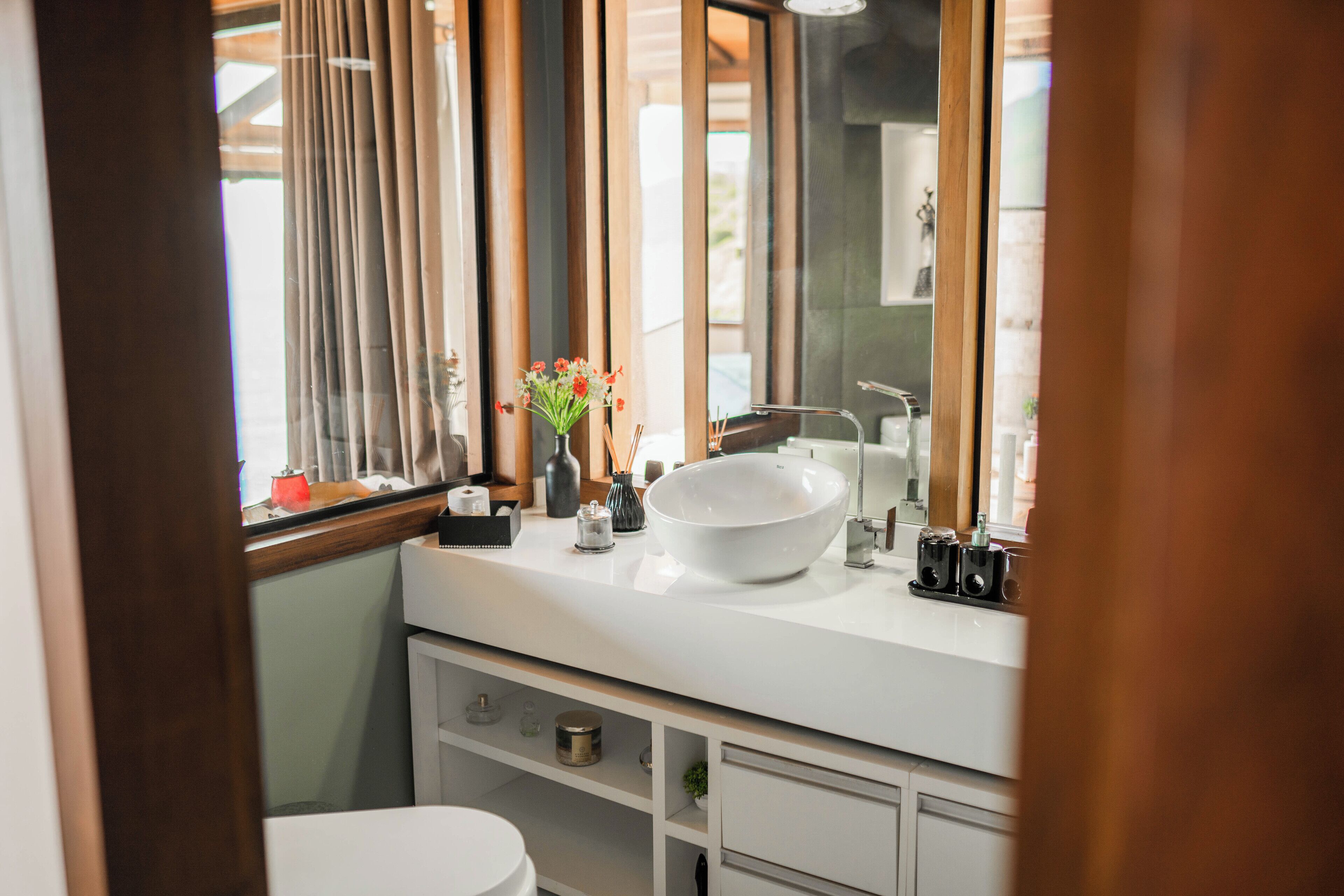 Een moderne badkamer met een groot wit wastafel, een spiegel en een raam met gordijnen.