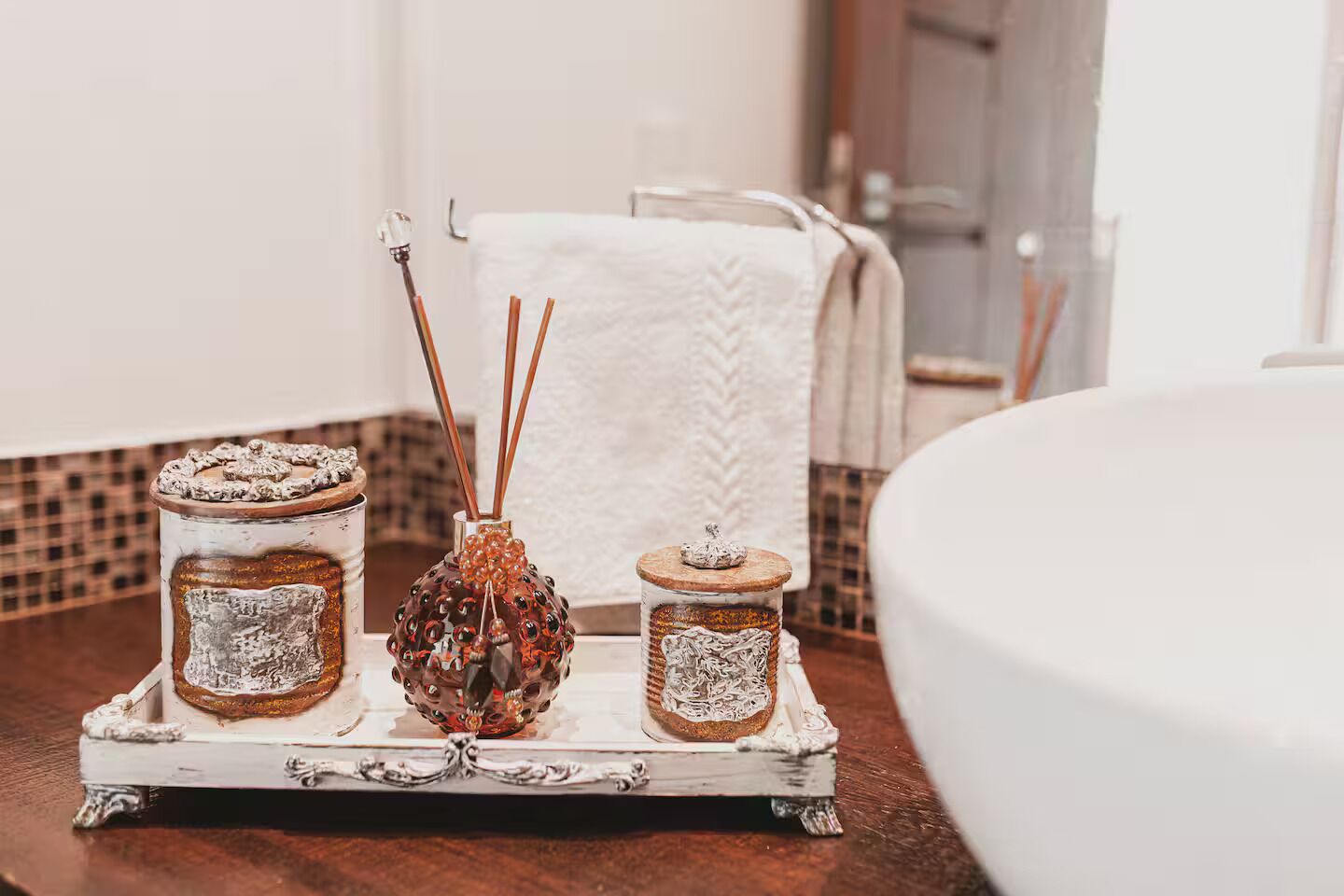 Une salle de bain avec un lavabo blanc, une serviette blanche et trois pots décoratifs disposés sur un plateau.
