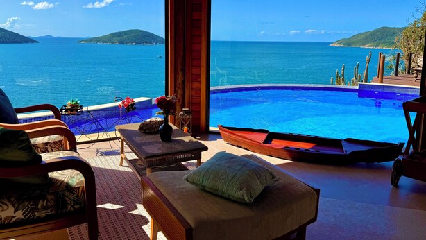 A room with a view of the sea, a pool, and wooden furniture. - Luxury Oceanfront Villa with Infinity Pool, Sauna & Total Privacy (Arraial do Cabo)