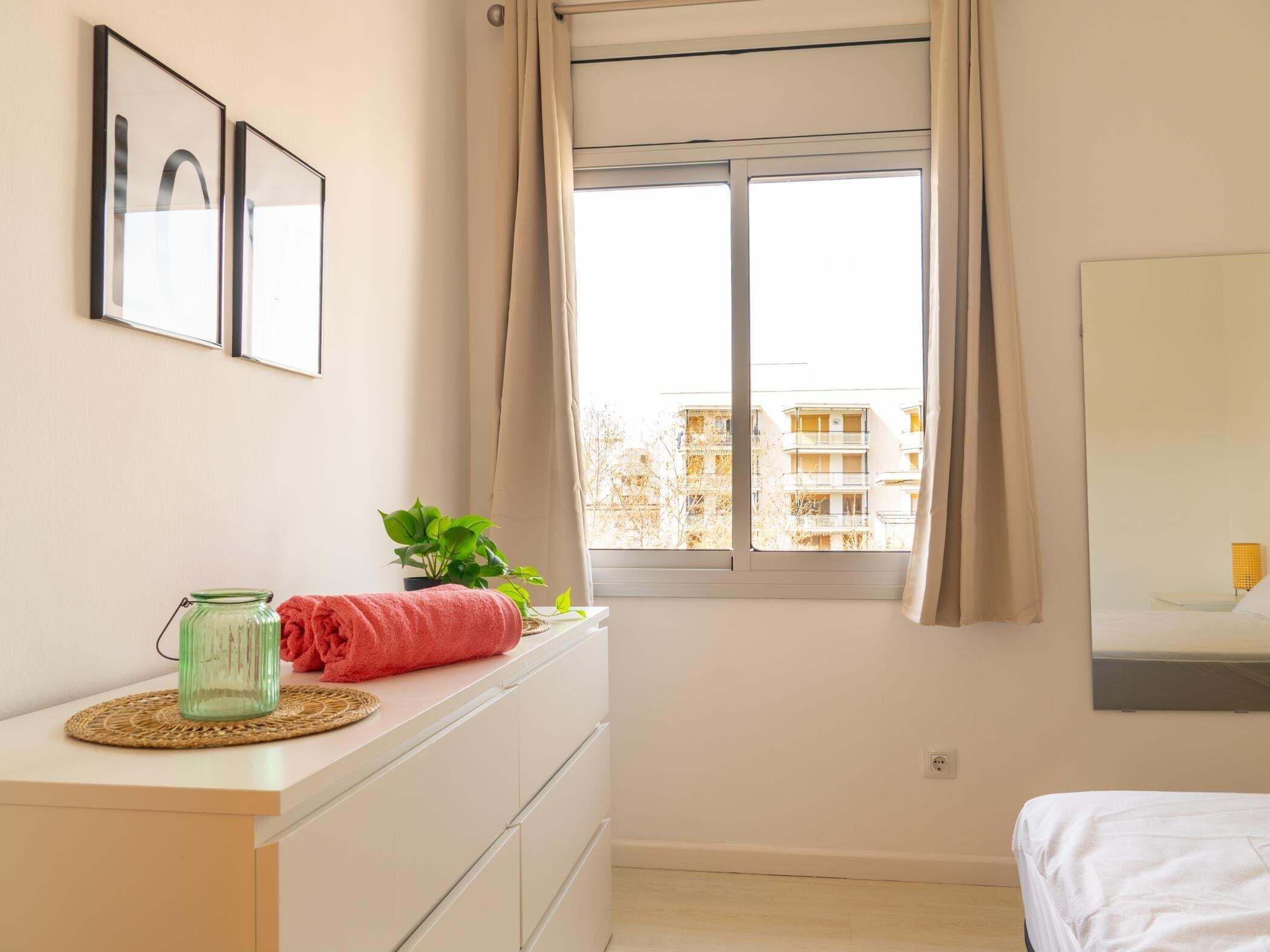 A bedroom with a bed, a dresser, a window with curtains, a plant, and a framed picture on the wall.