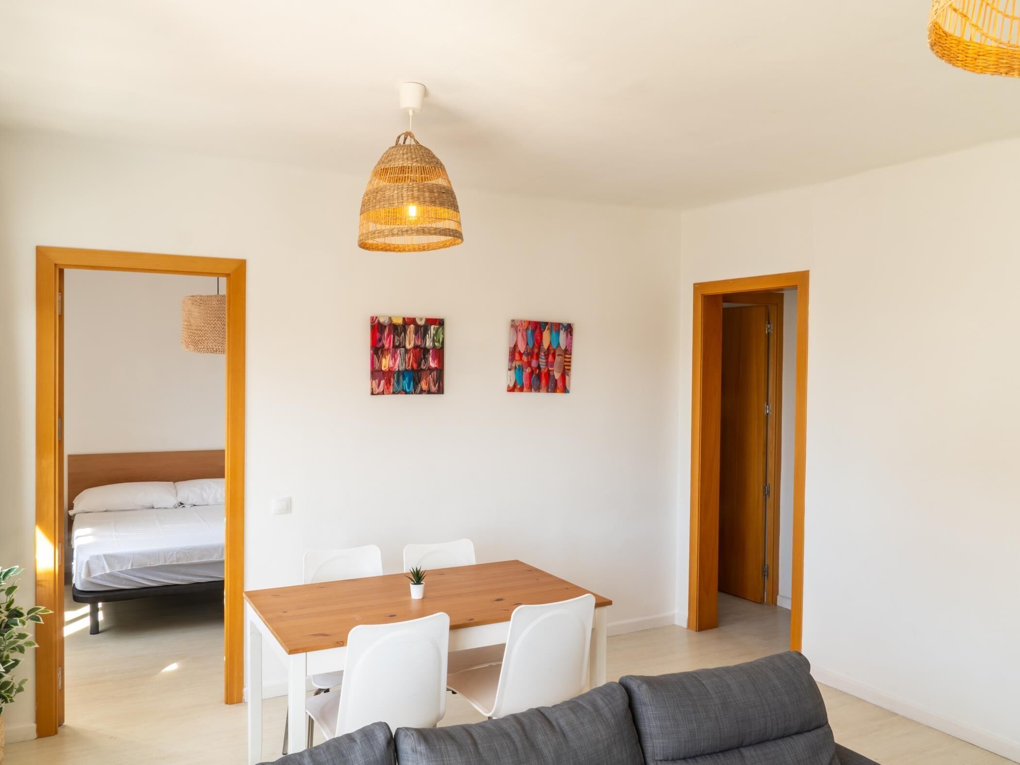 Ein modernes Zimmer mit einem Holzespeisetisch, weißen Stühlen, einem grauen Sofa und zwei farbenfrohen abstrakten Bildern an der Wand.