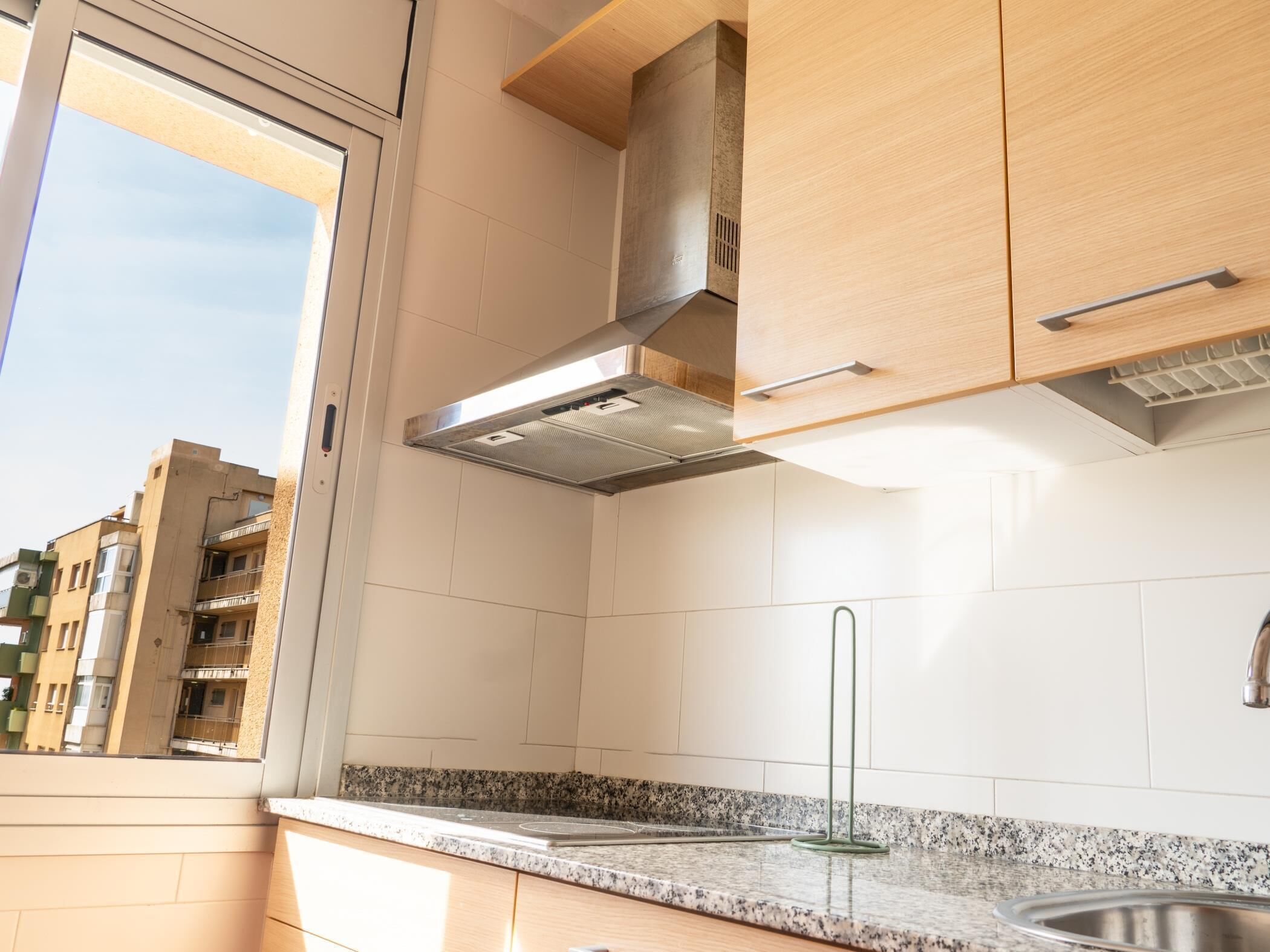 Eine moderne Küche mit weißen Schränken, einer Edelstahl-Spüle und einem Fenster mit Blick auf die Stadt.