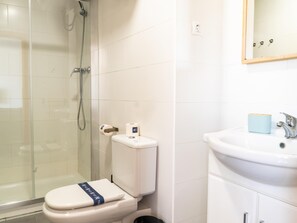 A bathroom with a glass shower enclosure, a toilet with a paper towel holder, and a sink with a mirror above it. - Apartament Corall 4B with seaview (Salou)