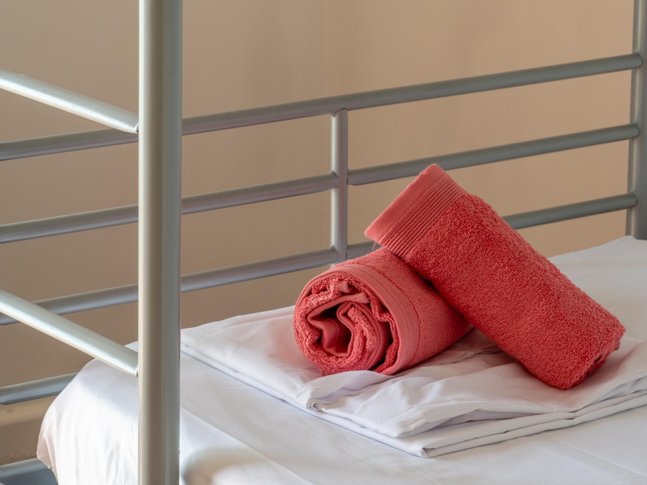 Een metalen bedframe met een witte matras en een opgerolde rode handdoek erboven.