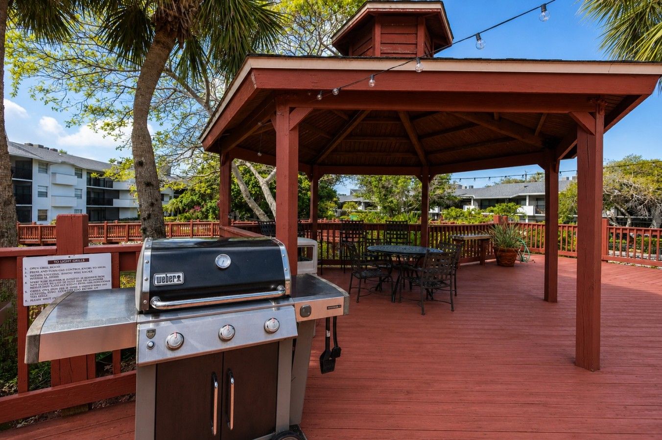 Ein Grillbereich im Freien mit einer Holzpergola, einem Tisch mit Stühlen und einem Schild mit der Aufschrift '10 LICHTE GRILLS'.