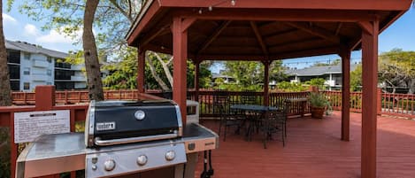 An outdoor grill area with a wooden pergola, a table with chairs, and a sign indicating '10 LIGHT GRILLS'.