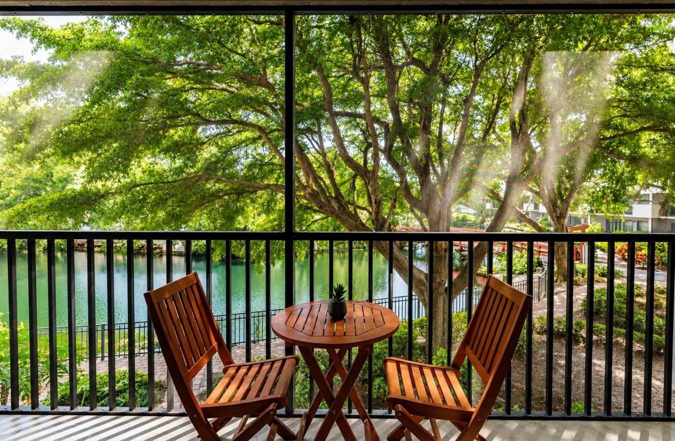 Un balcon avec une table et deux chaises, donnant sur une étendue d’eau et sur de la verdure.