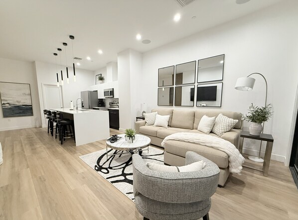 A modern living room with a sofa, a coffee table, and a dining area with chairs and a kitchen in the background. - NEW HIGH END LUXURY ARCADIA RETREAT 4BR/4BA PRIVATE ROOFTOP (Phoenix)