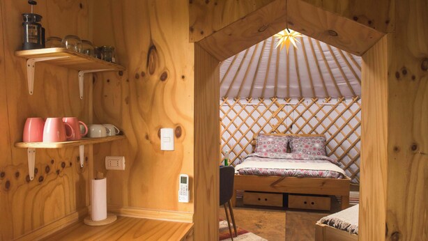 Une pièce chaleureuse en bois, avec un lit, des étagères remplies d’ustensiles de cuisine et une petite table.