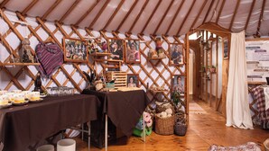 L’intérieur chaleureux d’une yourte, avec un coin repas, des étagères en bois où sont exposés des objets personnels et un tableau affichant le menu.